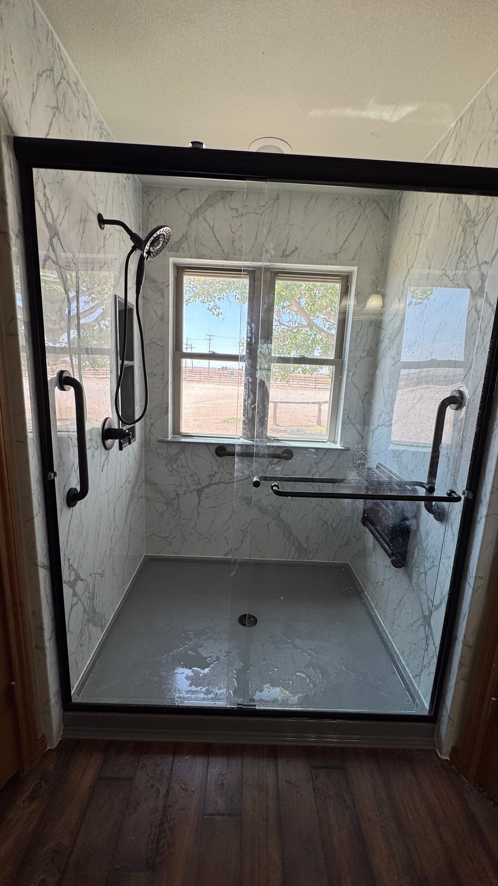 Marble-look walk-in shower with window and safety grab bars