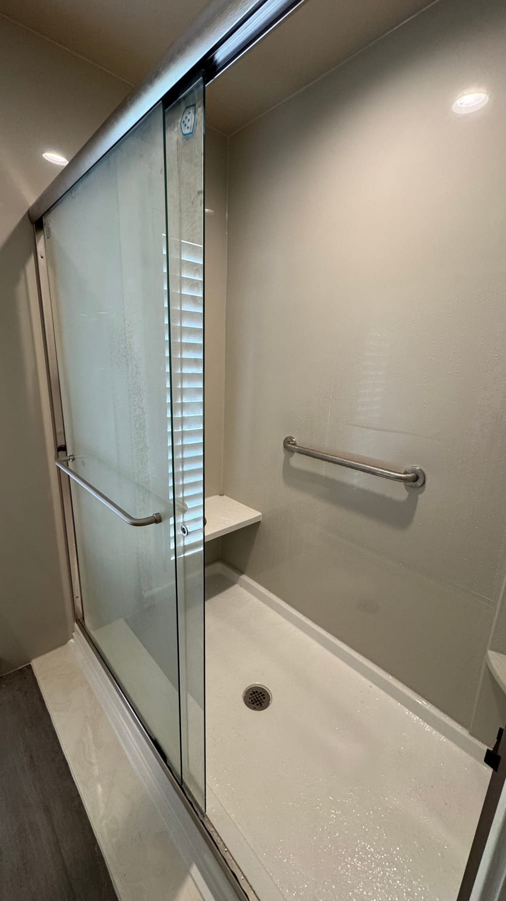 Accessible white shower with glass door, bench, and grab bars